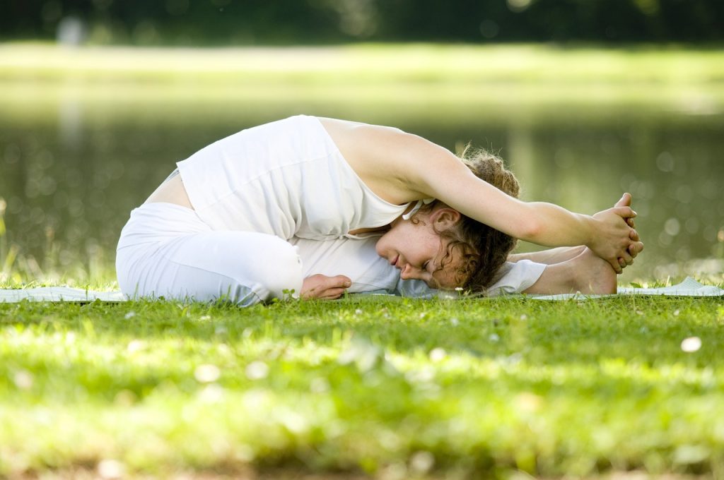 Mujer sentada en el suelo realizando un ejercicio de yoga que ayuda a estirar la espalda baja